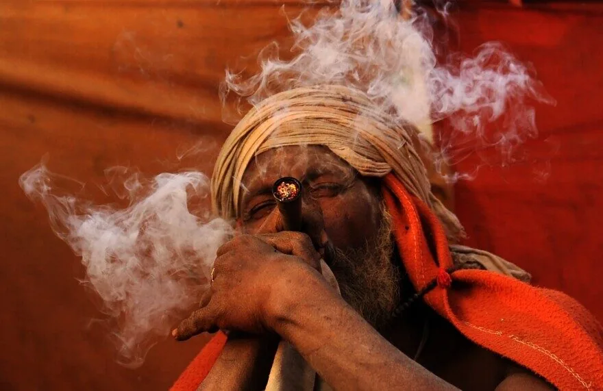 A sadhu in Nepal smoking a chillum, his face half-hidden in a cloud of white smoke.