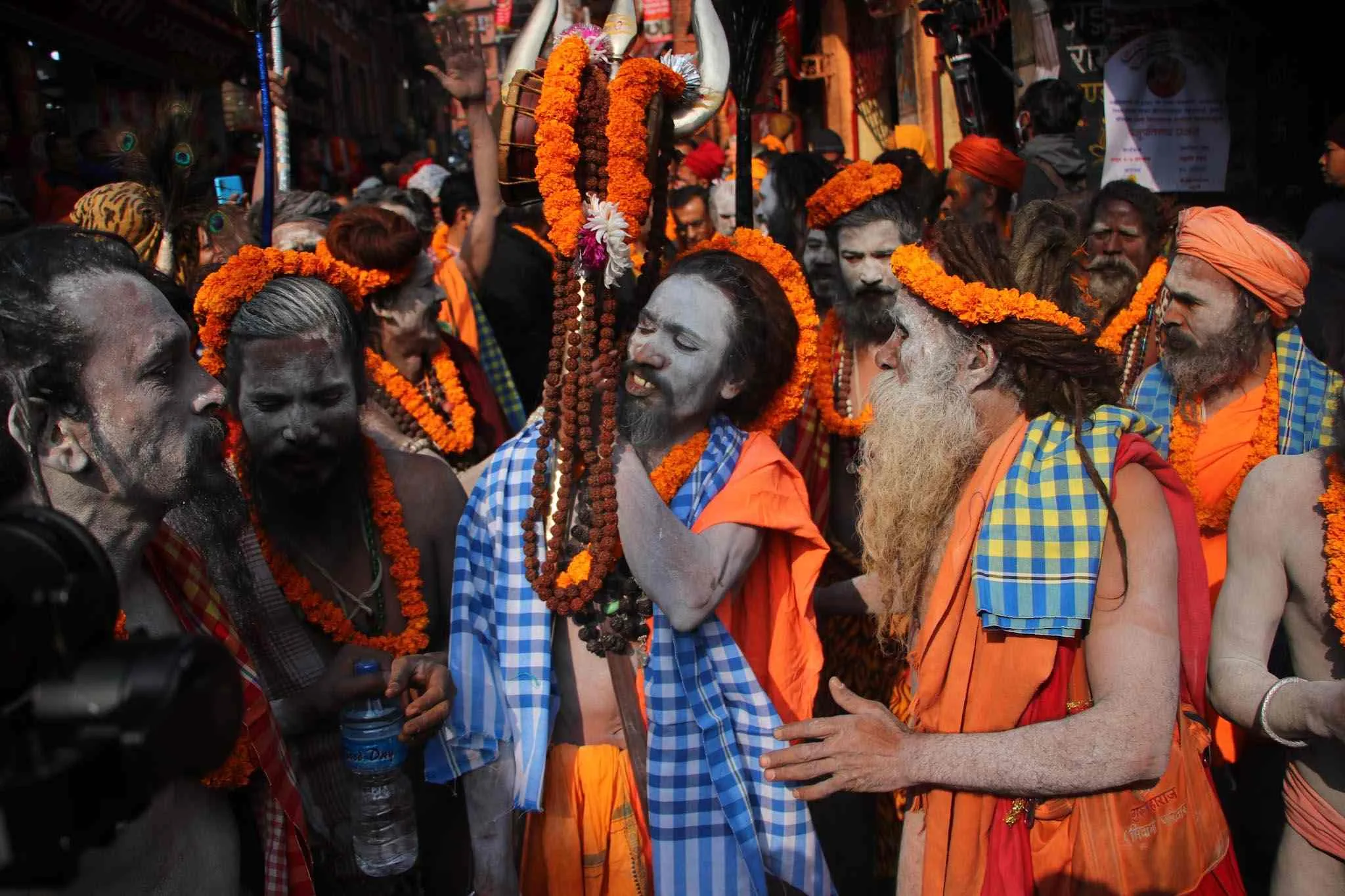 A dense crowd of Hindu sadhus wearing marigold garlands, ash-smeared faces, and orange robes, gathered during a religious festival.